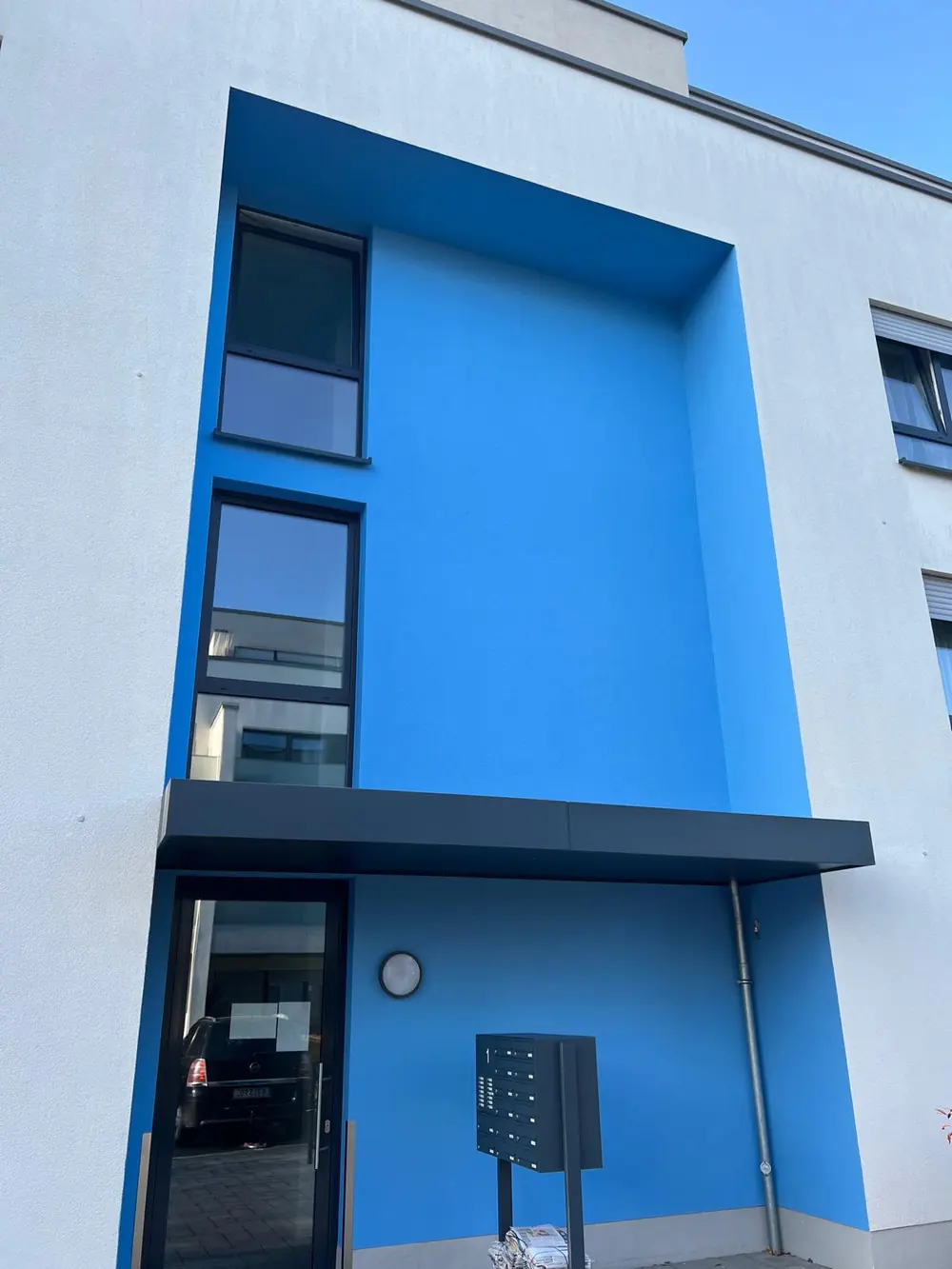 Mehrfamilienhaus mit neu gestrichener Fassade in Weiß und kräftigem Blau am Eingang